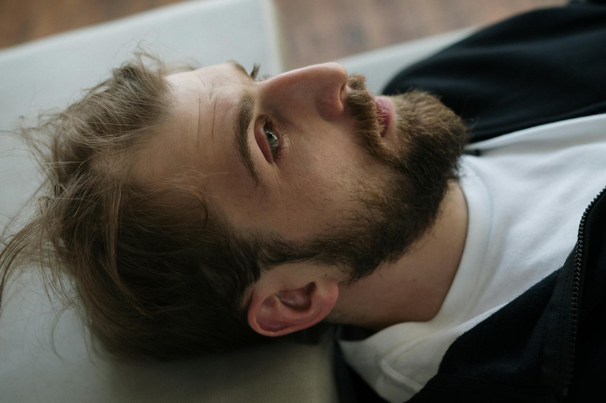 Close-up portrait of a bearded man lying down indoors, reflecting emotions and thoughts.